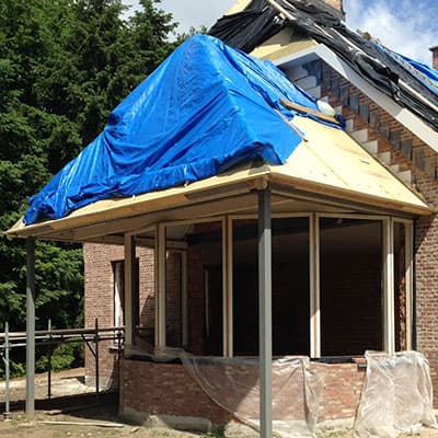 Aanbouw in aanbouw met houten dakconstructie onder een blauw dekzeil