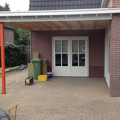 Overkapping met houten plafond boven een oprit, naast witte tuindeuren