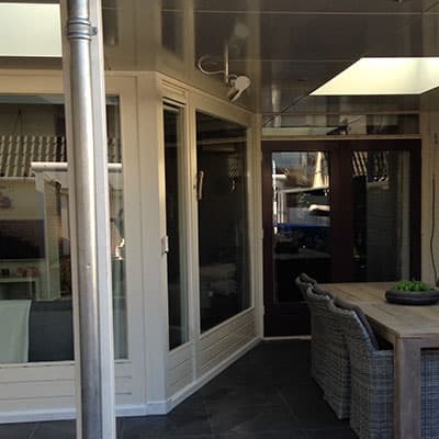 Overkapping met witte kozijnpuien en zicht op een tuinterras