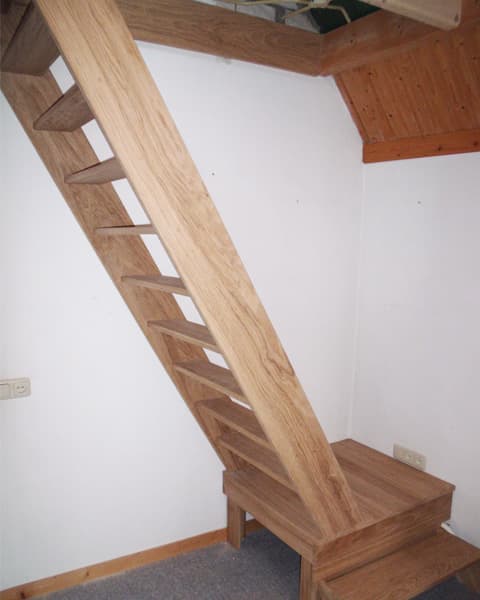 Steile eikenhouten trap tegen een witte wand onder een houten balk
