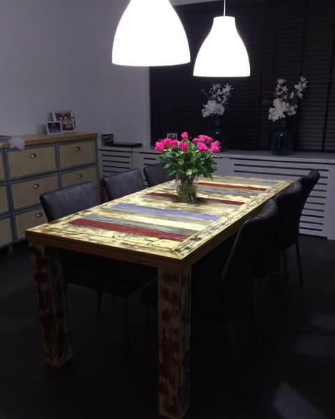 Eettafel van sloophout met gekleurde tafelloper onder twee hanglampen